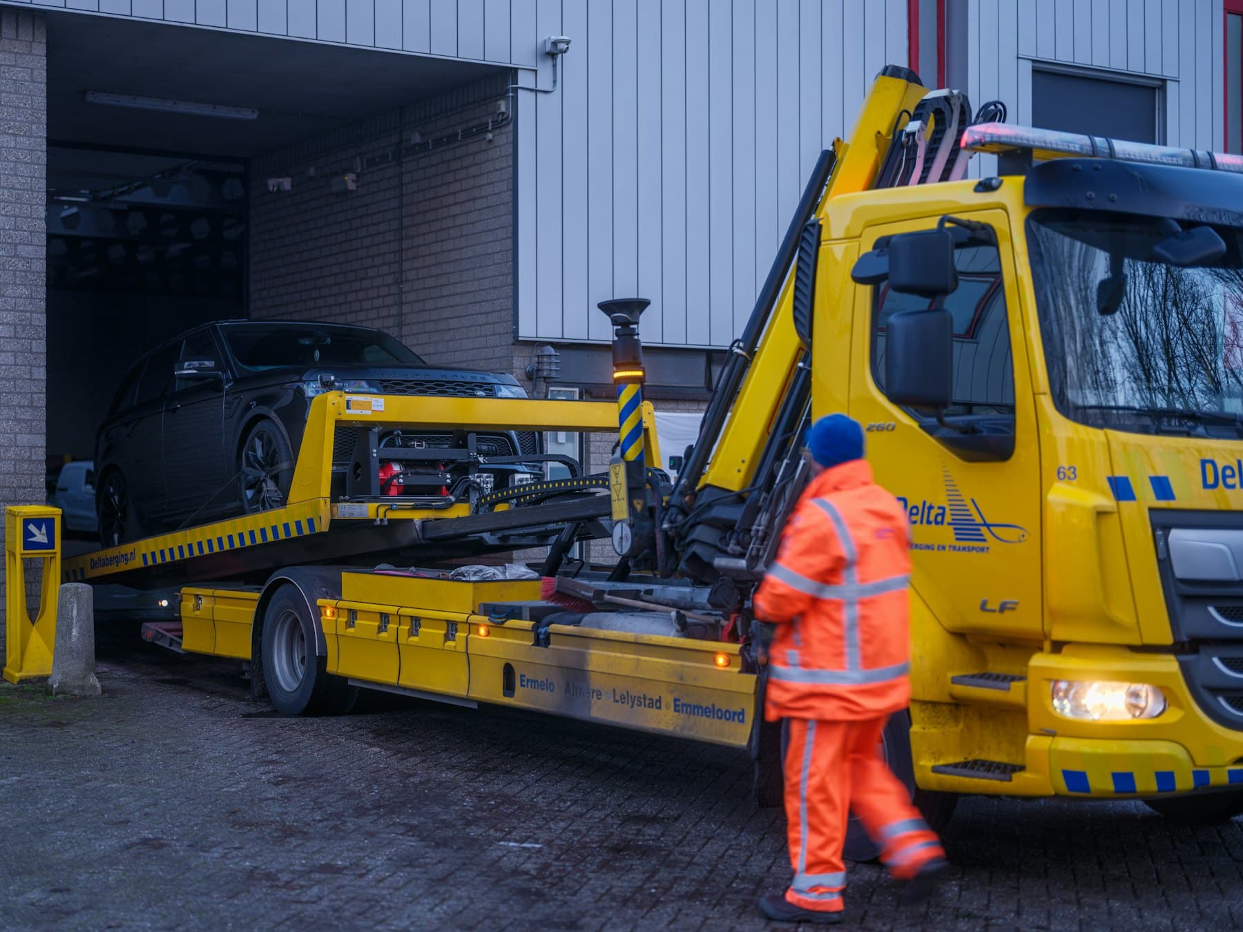 Un transporteur en tenue de sécurité prépare le chargement d’une voiture sur un camion plateau